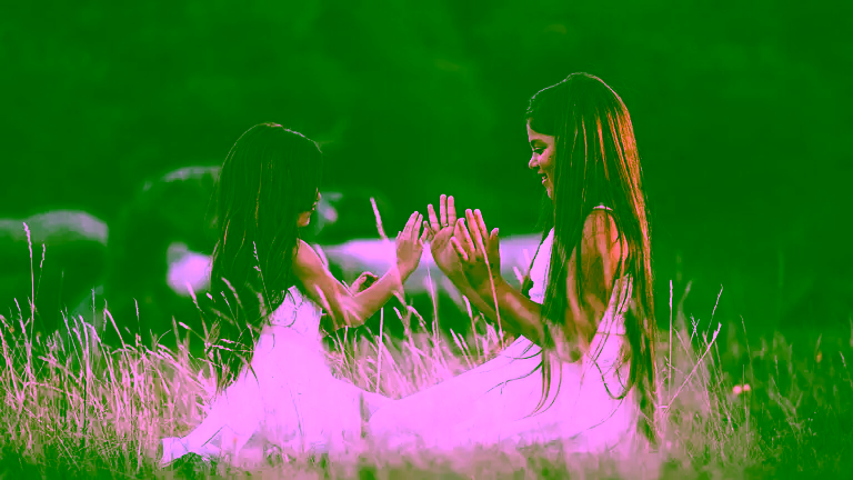 Intl-Friendship-Day Two young girlfriends playing paddycake in a field of tall grass.